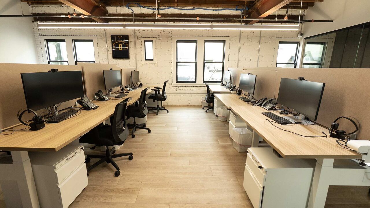 Two rows of sit-stand desks with large monitors and privacy panels, facing each other across an aisle